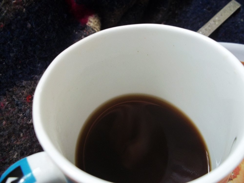 A cup of black coffee resting on dark fabric — the visual register of sonic seasoning