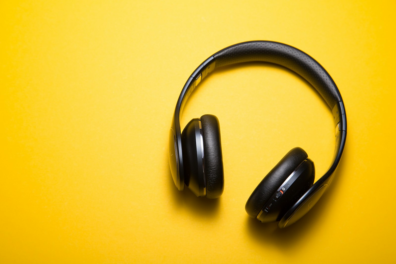 A pair of black over-ear headphones on a plain yellow ground — a single song, returned to until it becomes one's own