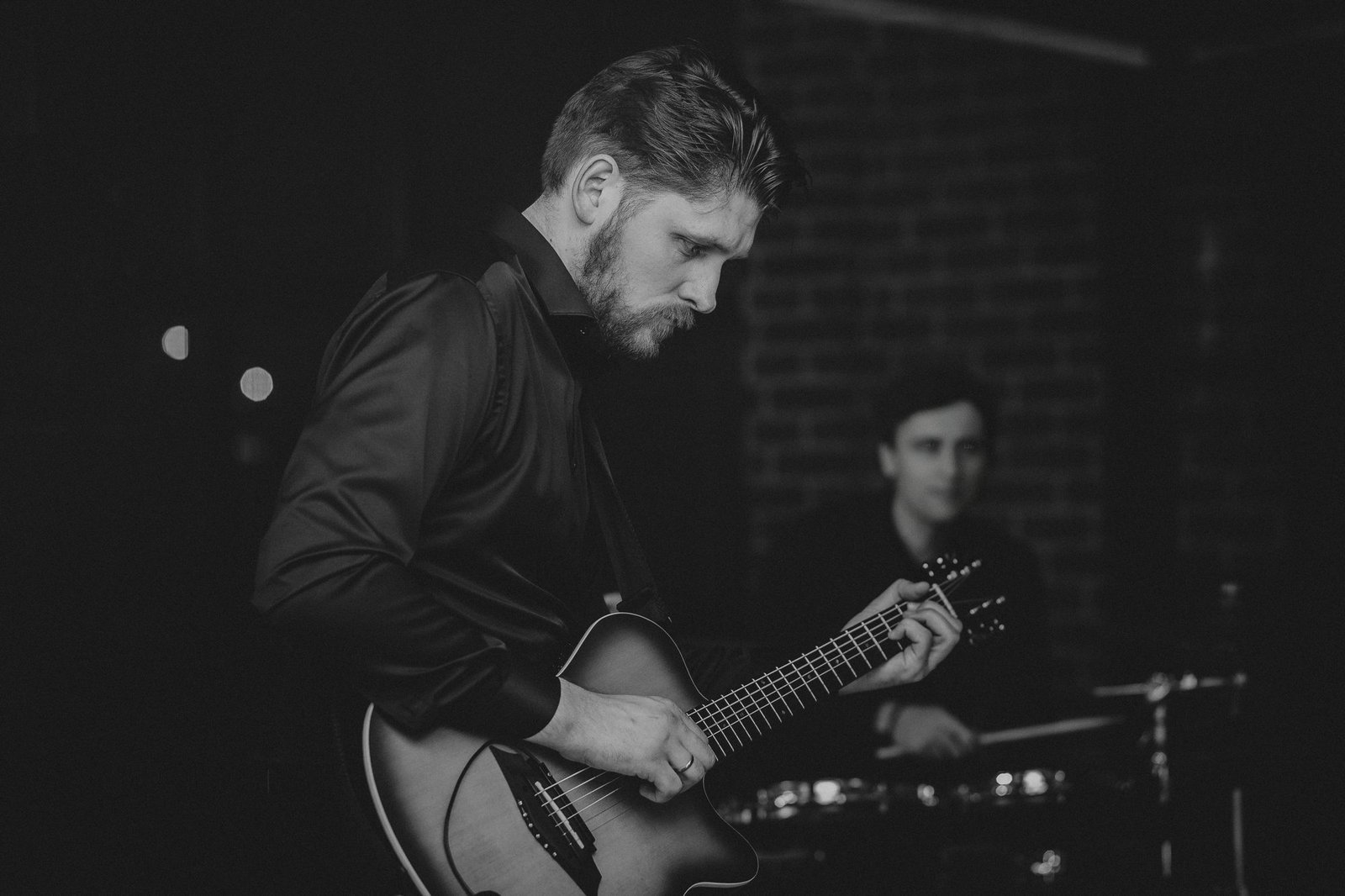 Justinas Stanislovaitis playing acoustic guitar in low stage light — black-and-white live photograph