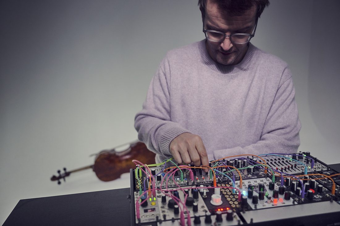 Peter Gregson verkabelt seinen Modularsynthesizer, hinter ihm ruht sein Cello