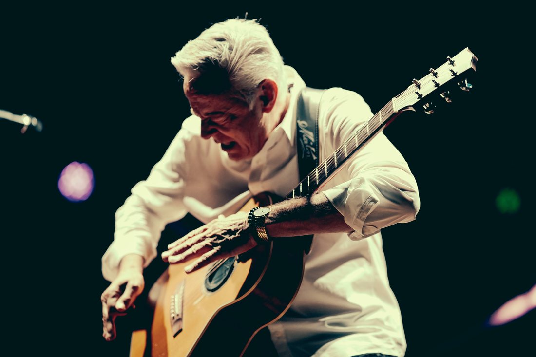 Tommy Emmanuel auf der Bühne, über seine Maton-Gitarre gebeugt, die rechte Hand auf dem Korpus, in dramatischem Licht