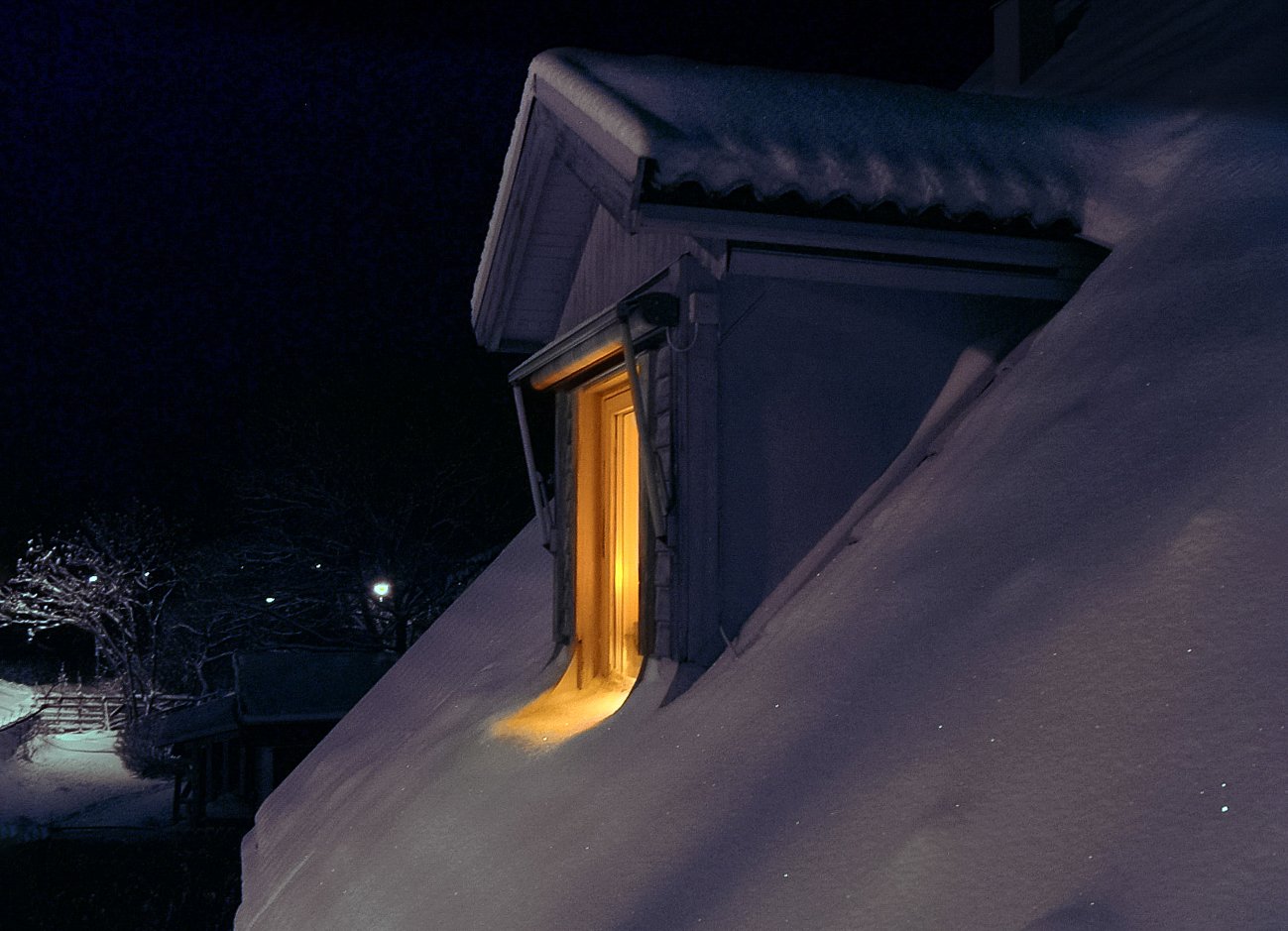 A warm-lit window in a snow-covered roof at night — the visual register of winter solitude
